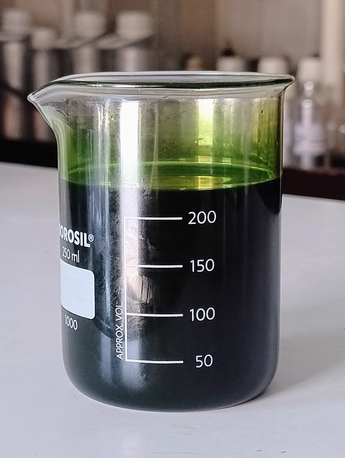 A beaker of dark green vetiver oil drawn off after distillation